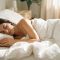 Woman resting peacefully in white linen bedding in soft morning light