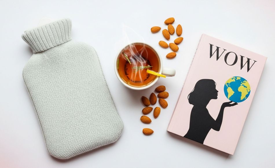 Ein Vorbereitungs-Set für Menstruationsbeschwerden mit Wärmflasche, Kräutertee und gesunden Snacks.