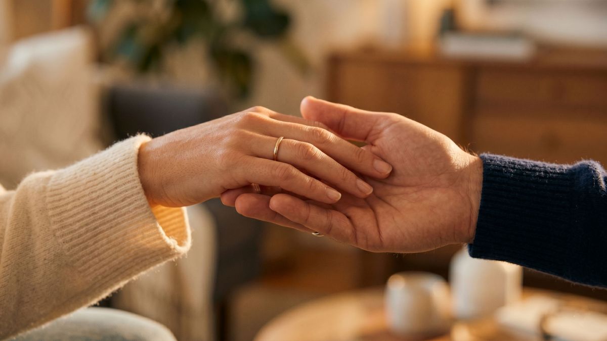 La mano de una mujer descansando suavemente sobre la mano de un hombre bajo una cálida luz tenue, expresando amor romántico a través del tacto.