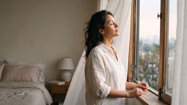 Mujer con lino color marfil junto a una ventana abierta bajo una suave luz matutina, ilustrando la ciencia natural del olor corporal femenino