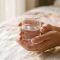 Manos de mujer sosteniendo un vaso de agua transparente bajo luz natural, representando la humedad e hidratación natural del cuerpo femenino — editorial de salud femenina