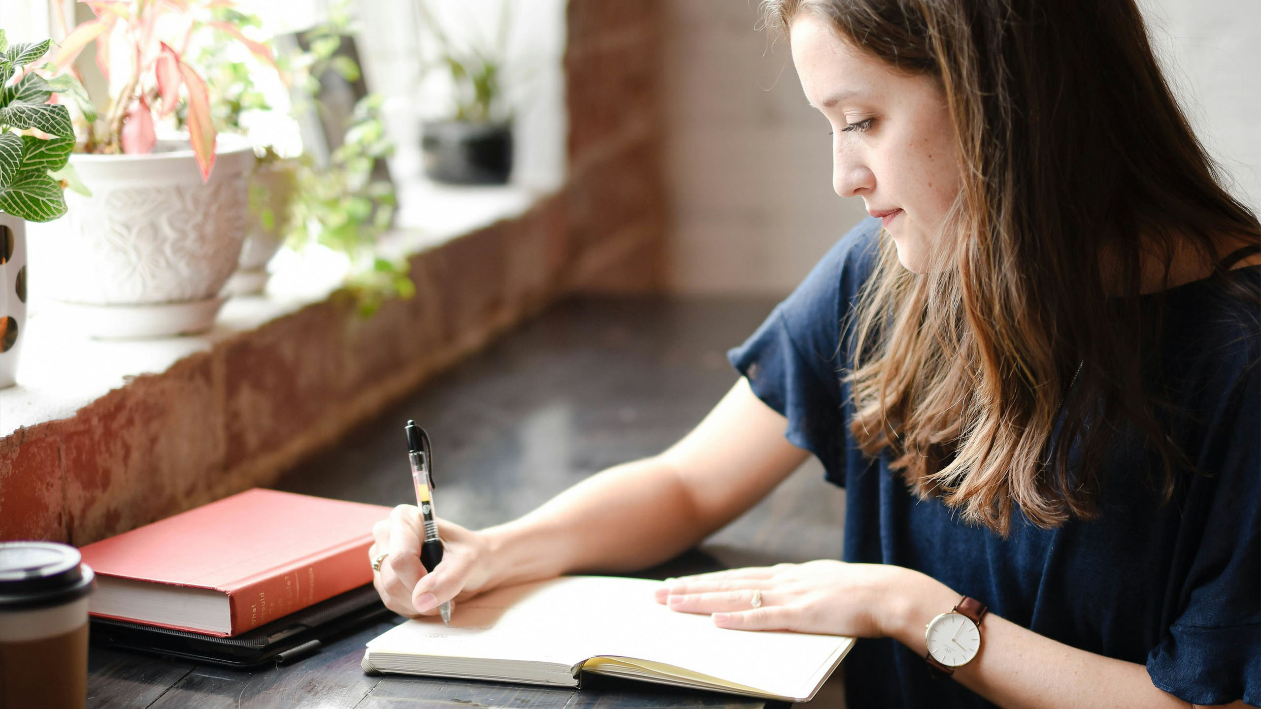 Mujer escribiendo en un diario junto a una ventana soleada para fortalecer su resiliencia emocional
