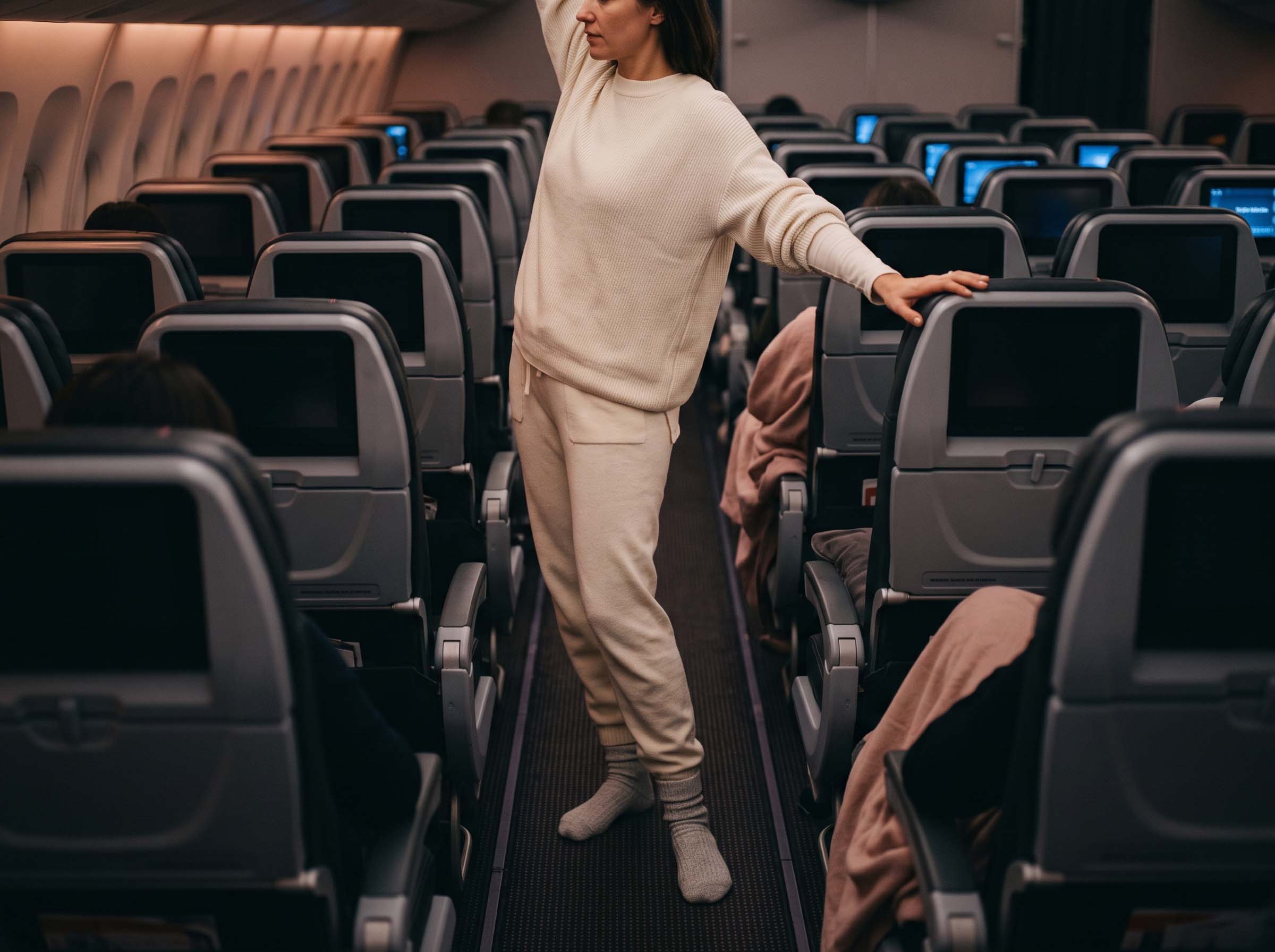 Mujer con prendas de punto suave de algodón descansando cómodamente en un asiento de ventana en un vuelo de larga distancia
