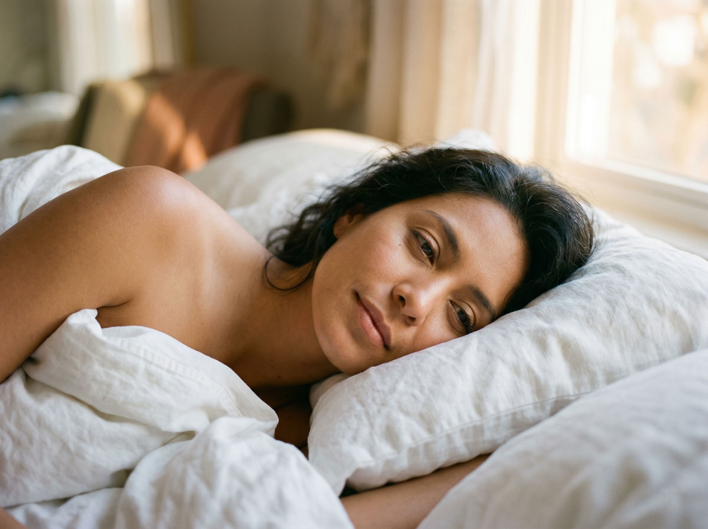 Mujer despertando pacíficamente con la suave luz de la mañana, sábanas de lino blanco