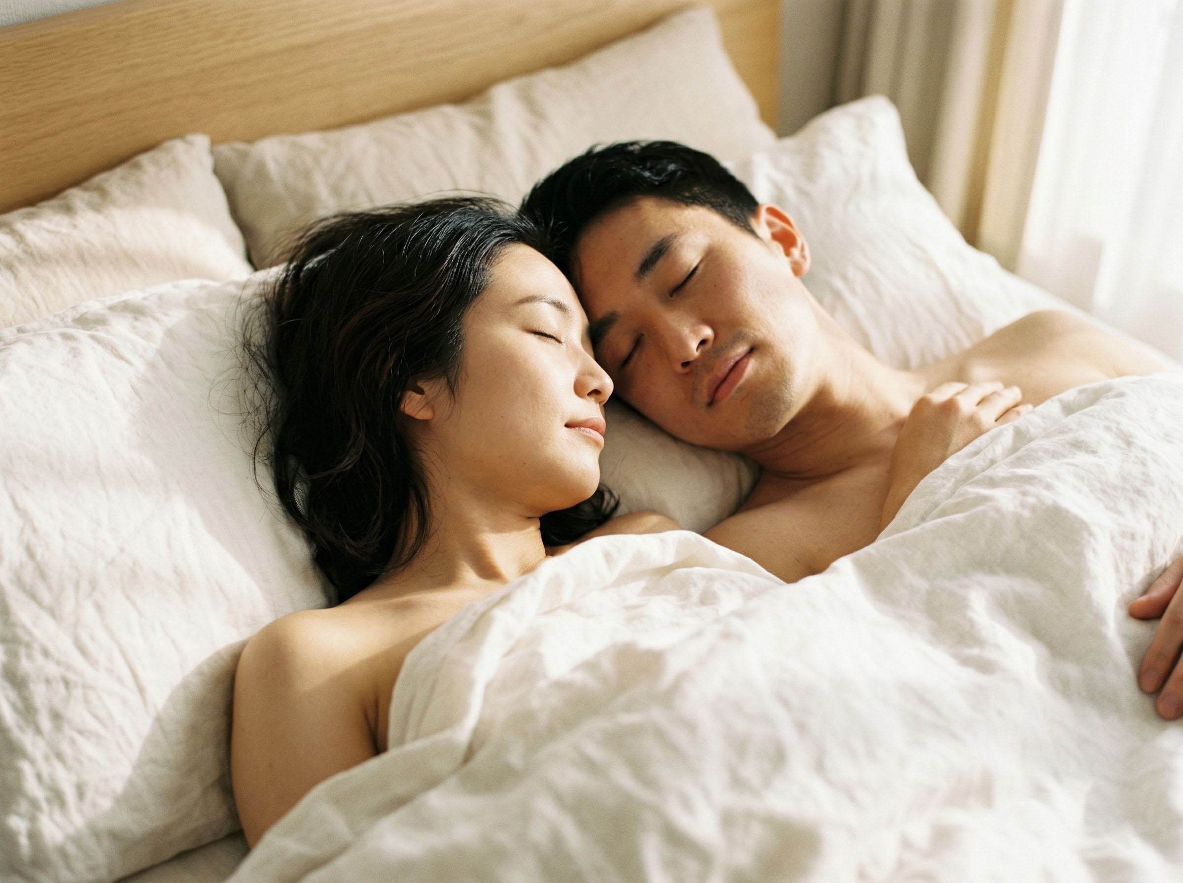 柔らかな白いリネンの下で穏やかに共に眠るカップル、温かな朝の雰囲気