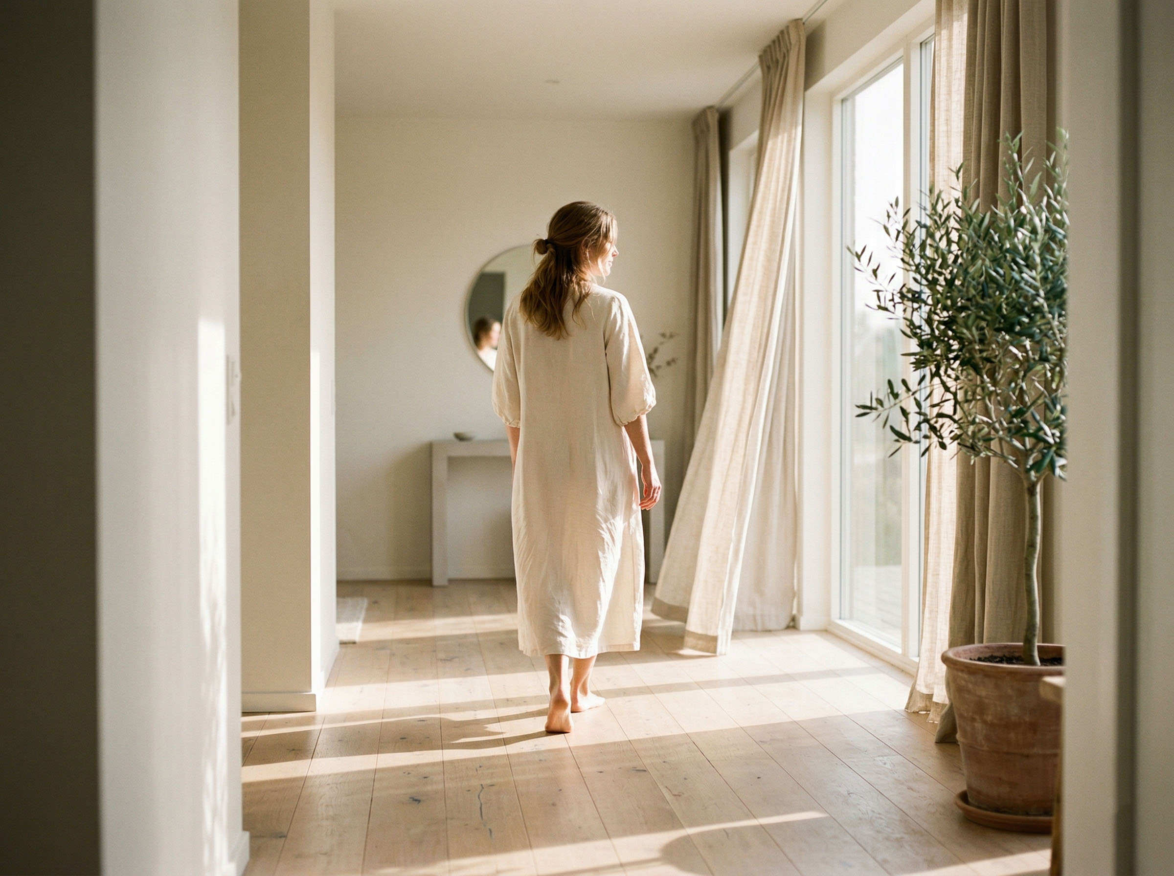 A woman in morning light moving through a sunlit home, a sense of ease and comfort in her own space