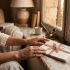 Manos de una mujer descansando junto a cartas de amor escritas a mano bajo la suave luz de una ventana, representando la historia de la anticipación romántica.