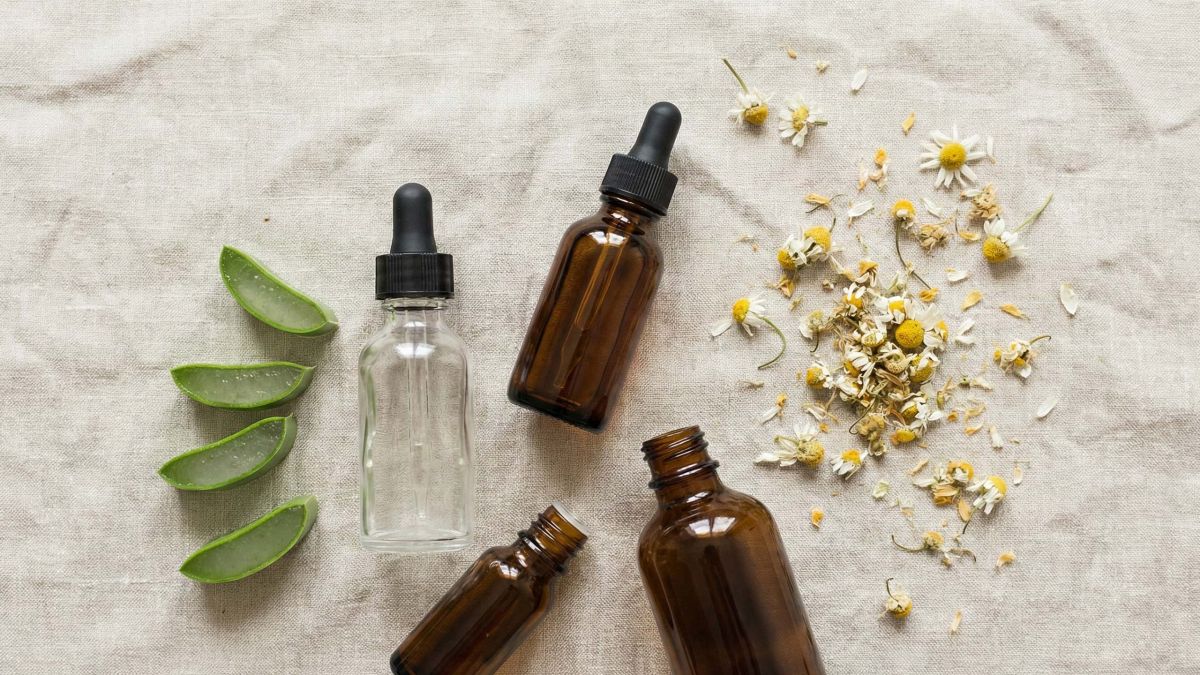 Une collection d'ingrédients de soin naturels comprenant de l'aloe vera, de la camomille et des huiles botaniques sur une surface en lin rose clair.