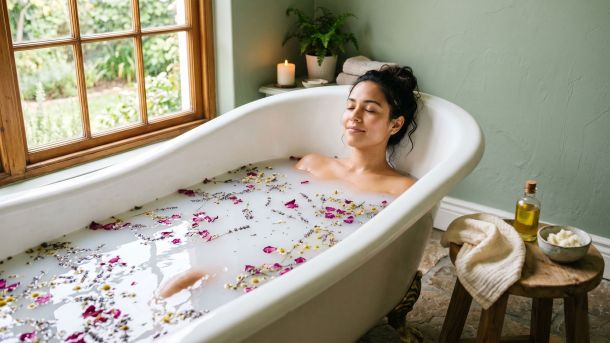 Mujer relajándose en un baño rodeada de plantas naturales y flores de temporada.