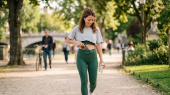 Une femme en legging vert sauge glisse son smartphone dans sa ceinture lors d’une promenade.