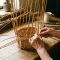 Close-up of a woman's hands skillfully weaving a natural willow basket in a sunlit room.