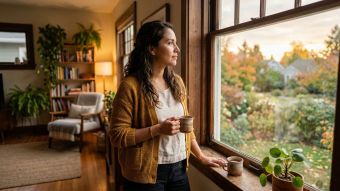Una mujer pensativa mirando por una ventana en un hogar cálido.
