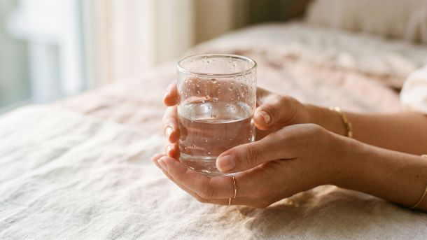 Woman's hands holding a clear glass of water in natural light, representing the female body's natural moisture and hydration — women's health editorial