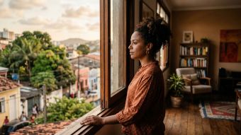 Uma mulher pensativa olhando pela janela em um ambiente doméstico acolhedor.