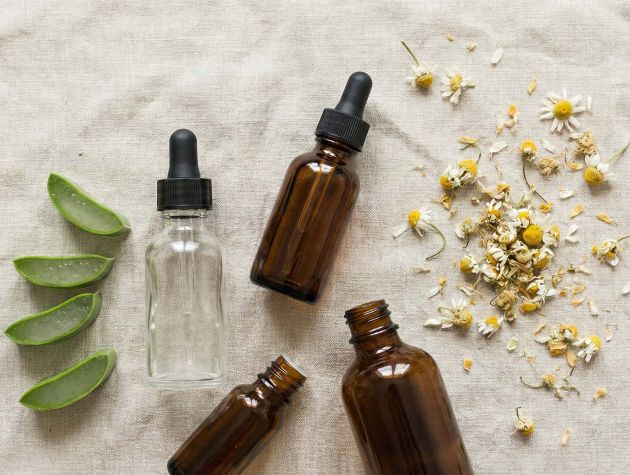 Eine Sammlung natürlicher Hautpflege-Inhaltsstoffe wie Aloe Vera, Kamille und botanische Öle auf einer hellrosa Leinenoberfläche.