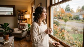 A thoughtful woman looking out a window in a warm home setting.