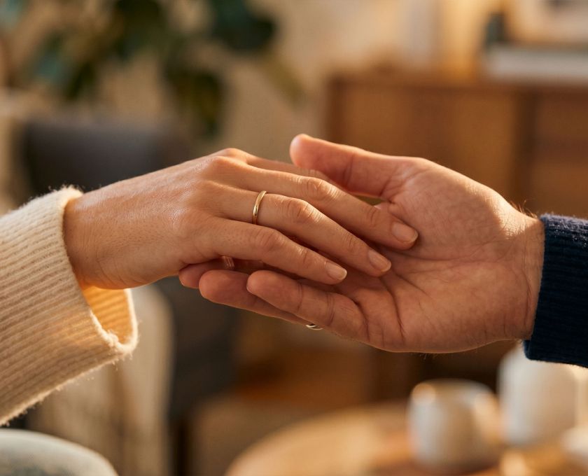 A woman's hand gently resting in a man's hand in soft warm light, expressing romantic love through touch