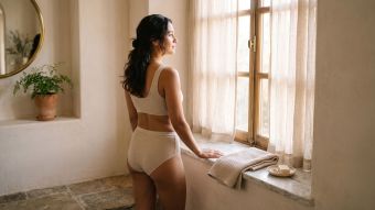 Mujer de pie junto a una ventana iluminada por el sol en el baño durante su tranquila rutina matutina después de la ducha