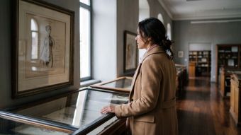 Mulher usando casaco cor de camelo observando uma gravura anatômica do século XIX emoldurada em um arquivo de museu, ilustrando a história de como a anatomia feminina era representada