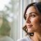 A woman with a serene expression looking out a window, representing a moment of self-acceptance and peace.