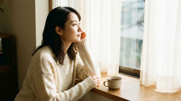 穏やかな陽光に包まれた部屋で物思いにふける女性。感情的な安らぎと女性的な優雅さを象徴している。