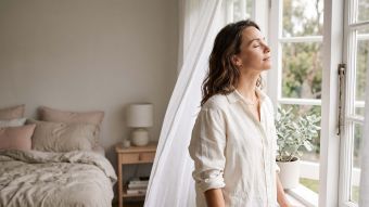 Woman in ivory linen at an open window in soft morning light, illustrating the natural science of female body scent