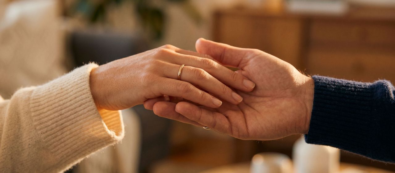 A woman's hand gently resting in a man's hand in soft warm light, expressing romantic love through touch