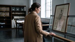 Woman in a camel coat viewing a framed nineteenth-century anatomical engraving in a museum archive, illustrating the history of how female anatomy was drawn