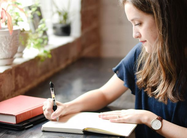 Mujer escribiendo en un diario junto a una ventana soleada para fortalecer su resiliencia emocional