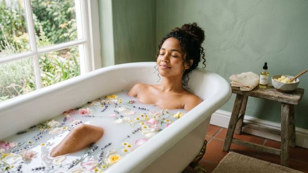 Mulher relaxando em um banho cercada por plantas naturais e flores sazonais.
