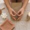 Woman's hands resting in a meditation mudra beside mala beads, a white flower, and a candle on a linen surface