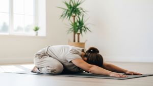 Una mujer en un entorno tranquilo realizando un suave estiramiento de la postura del niño sobre una esterilla de yoga para fomentar la conexión mente-cuerpo.