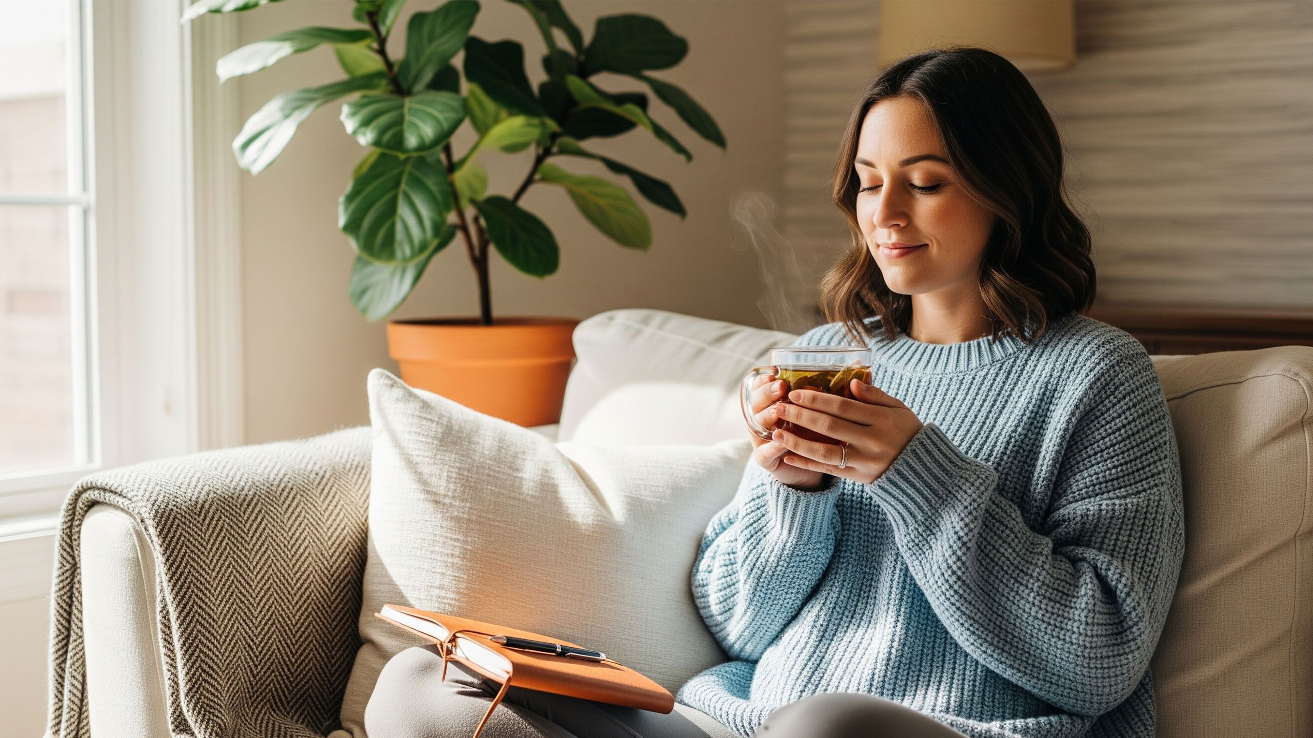 Una mujer relajándose cómodamente con una bebida caliente, simbolizando la práctica de crear rituales de descanso para cada fase del ciclo menstrual.