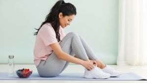 Femme lace ses chaussures près de fruits et d’eau—habitudes équilibrées et durables